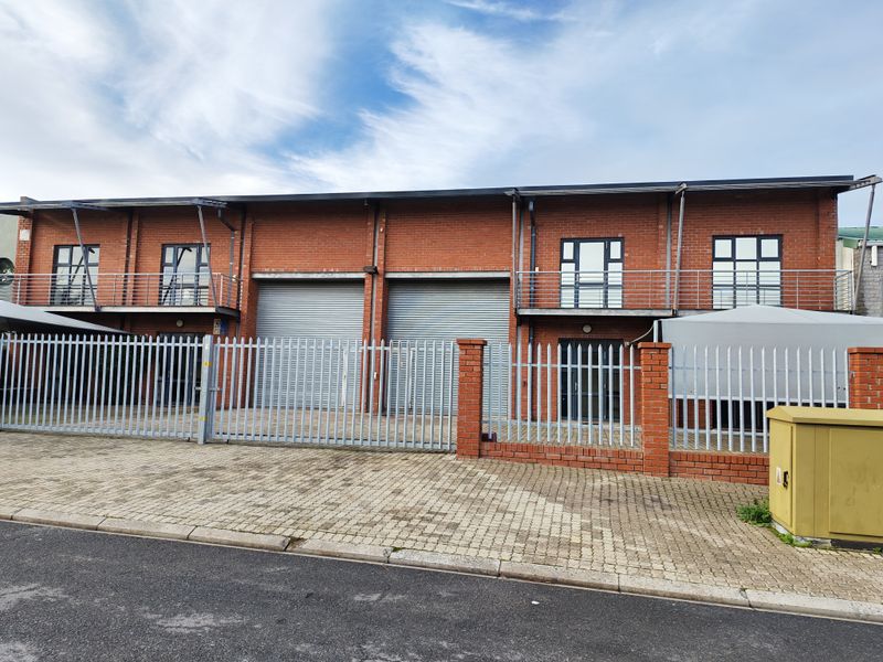 Front exterior view of an industrial property featuring brick facade, roller shutter doors, and secure metal fencing with a paved driveway.