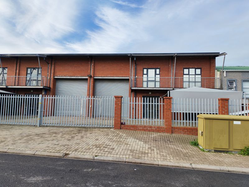 Front elevation of an industrial property featuring red brick construction, roller shutter doors, and secure metal perimeter fencing.