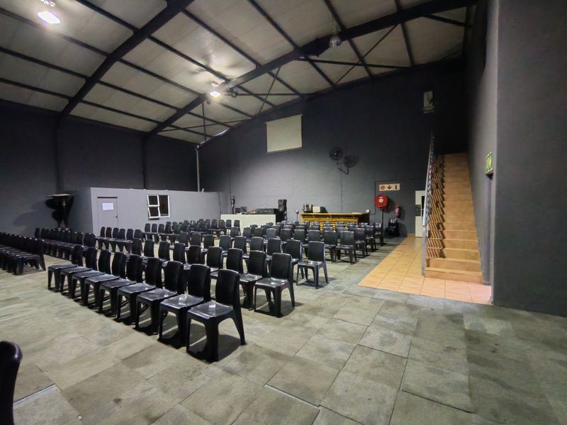 Spacious industrial open-plan area featuring exposed steel roof trusses, tiled flooring, and a built-in bar counter with an adjacent staircase.