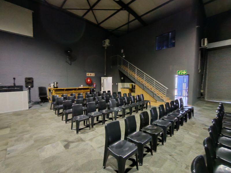Spacious industrial open-plan area featuring exposed steel roof trusses, a staircase with metal railing, and a large roller shutter door.