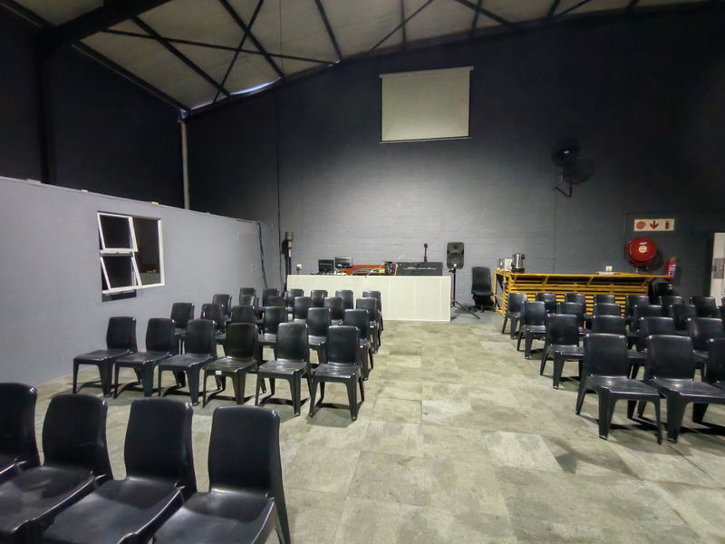 Spacious industrial utility area featuring high ceilings with exposed steel trusses, tiled flooring, and a built-in service counter, suitable for events or multi-purpose use.