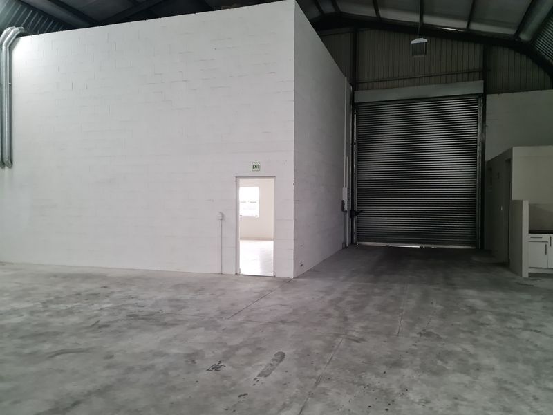 Spacious industrial warehouse unit featuring high ceilings, a large roller shutter door, and durable concrete flooring, suitable for various commercial or storage operations.