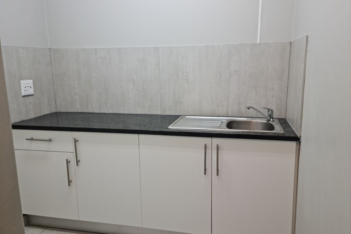 A clean, modern kitchenette featuring white built-in cabinetry, a dark granite countertop, and a stainless steel sink with a mixer tap.