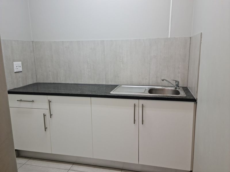A clean, modern kitchenette featuring white built-in cabinetry, a dark granite countertop, and a stainless steel sink with a mixer tap.