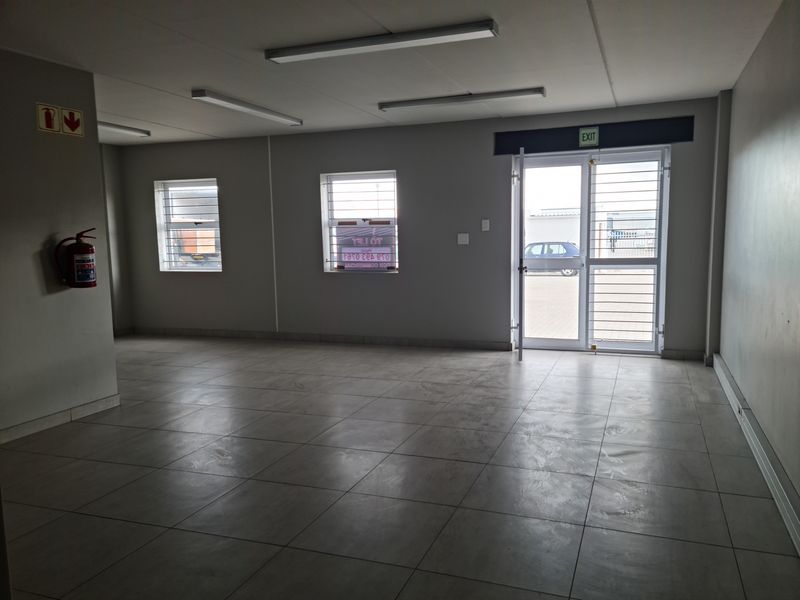 A clean, open-plan industrial office space featuring tiled flooring, fluorescent lighting, and secure access points with security bars.