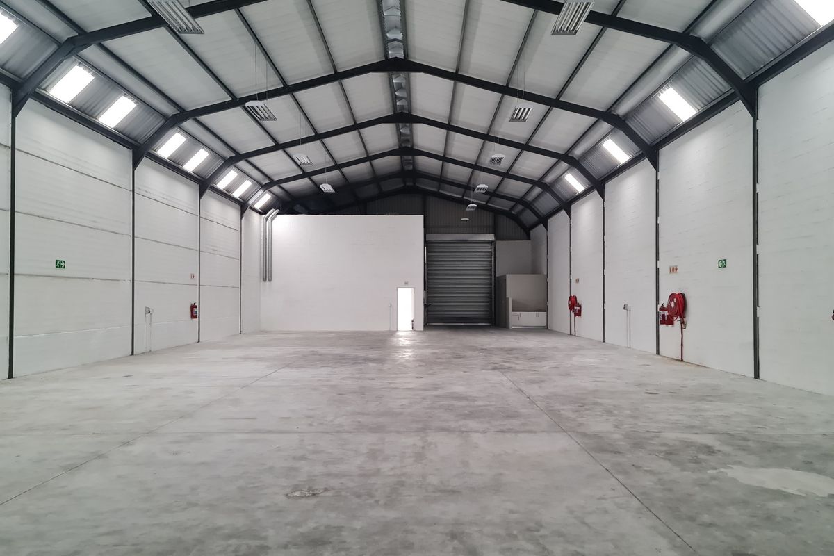 Spacious industrial warehouse featuring a high-clearance steel portal frame, concrete flooring, roller shutter access, and integrated fire safety equipment.