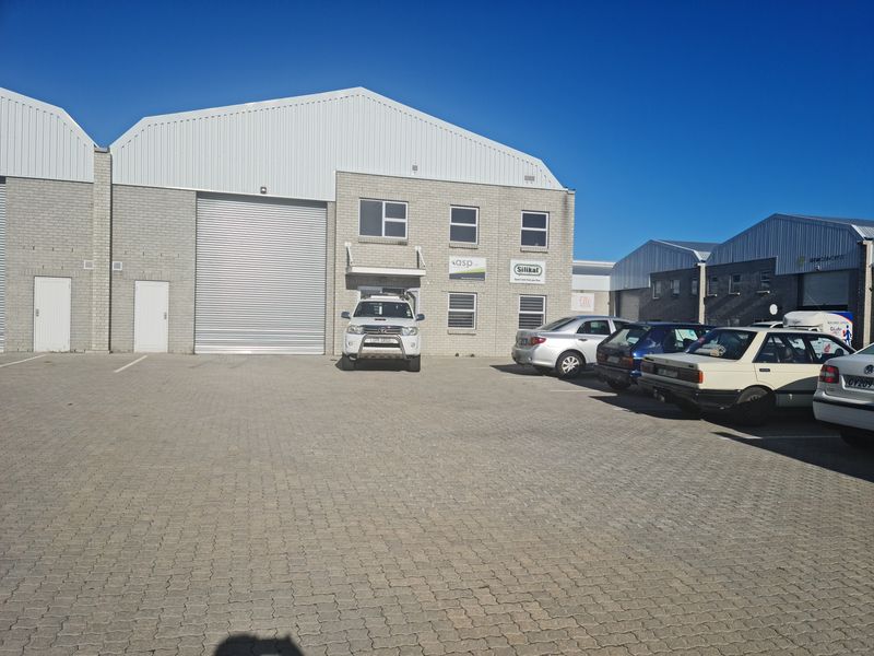 Front exterior view of an industrial warehouse unit featuring a large roller shutter door and paved parking area.