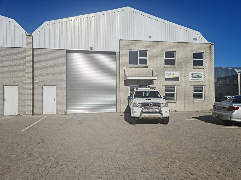 Front elevation of an industrial warehouse unit featuring a large roller shutter door, brick facade, and dedicated paved parking space.
