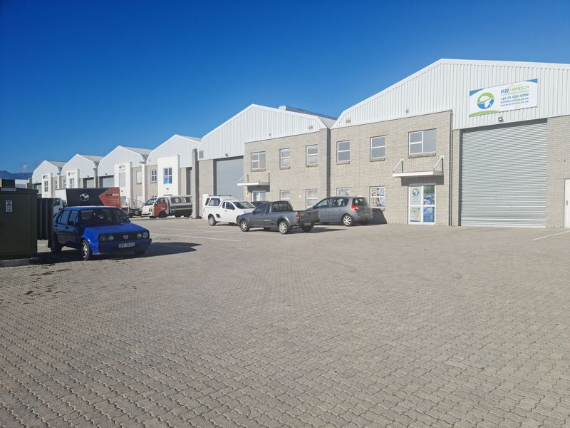 Front view of an industrial park featuring multiple warehouse units with roller shutter doors and a large paved parking area.