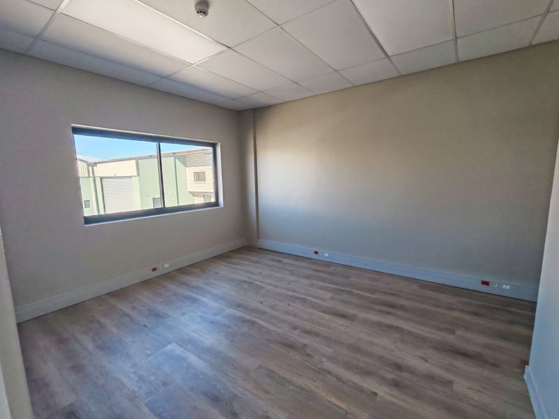 A clean, empty office space featuring laminate flooring, a suspended ceiling, and a large sliding window providing natural light.