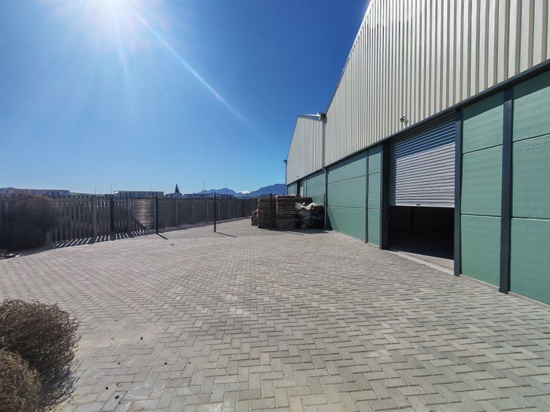 Industrial exterior rear yard featuring paved surfacing, perimeter fencing, and a large roller shutter door access point to the warehouse facility.