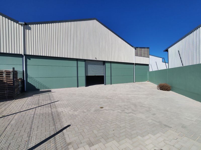 Industrial warehouse exterior featuring a paved yard, secure boundary wall with electric fencing, and a functional roller shutter door access point.