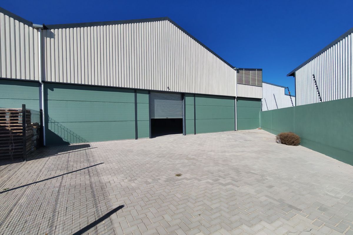 Industrial warehouse exterior featuring a paved yard, secure boundary wall with electric fencing, and a functional roller shutter door access point.