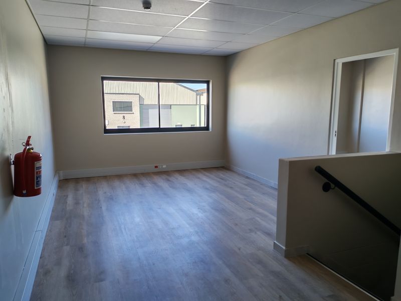 A clean, vacant office space featuring laminate flooring, a suspended ceiling, and a staircase with a handrail, suitable for professional use.