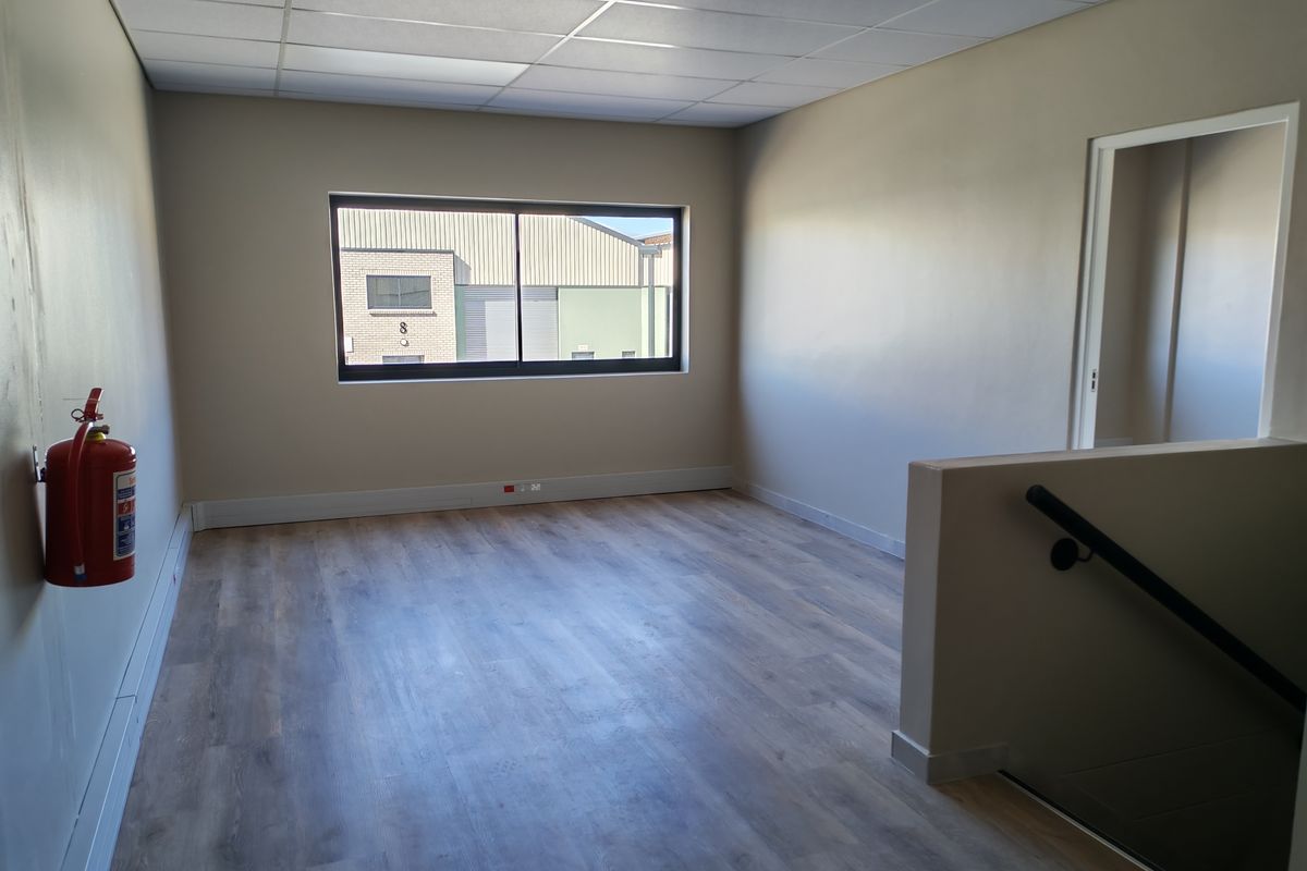A clean, vacant office space featuring laminate flooring, a suspended ceiling, and a staircase with a handrail, suitable for professional use.