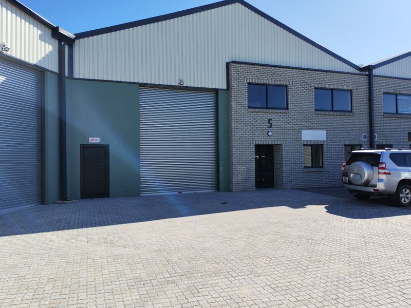 Modern industrial unit featuring a large roller shutter door, brick and metal cladding facade, and a paved driveway entrance.
