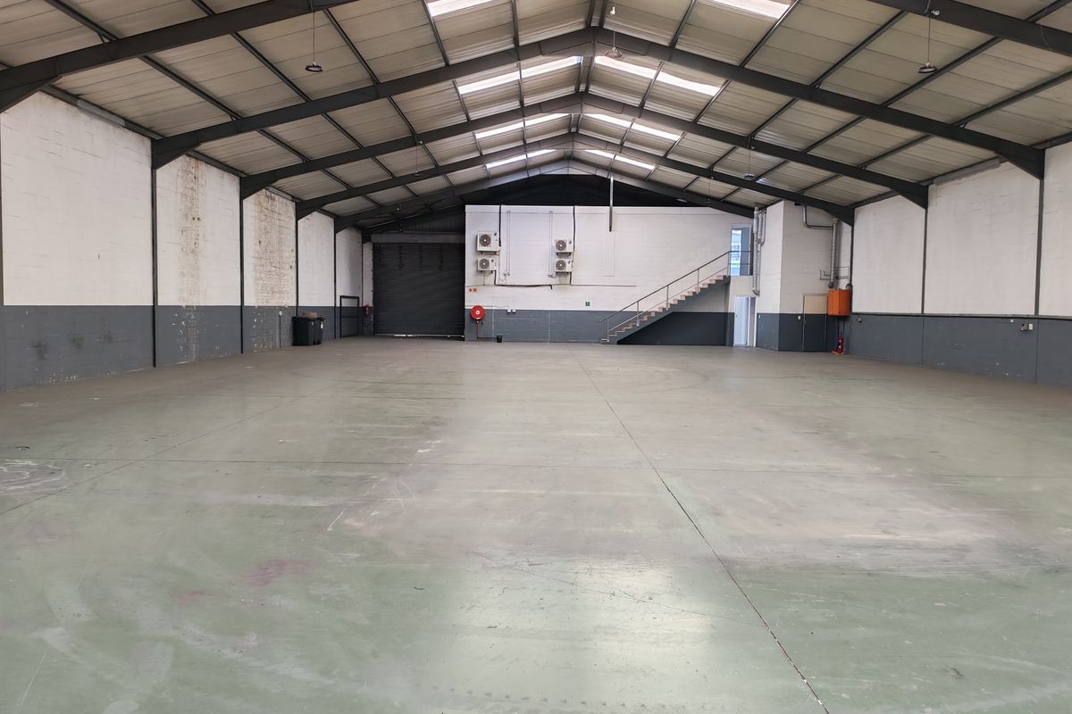Spacious industrial warehouse featuring a high-clearance steel portal frame, concrete flooring, roller shutter access, and integrated wall-mounted air conditioning units.