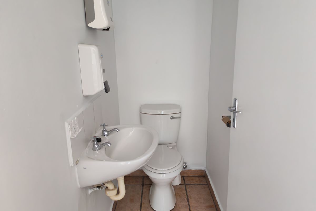 A functional industrial-style restroom featuring a standard toilet, wall-mounted washbasin, and tiled flooring.