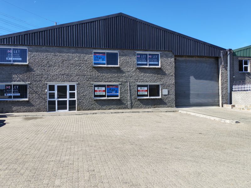Front elevation of an industrial property featuring a large roller shutter door, brick facade, and paved driveway area.