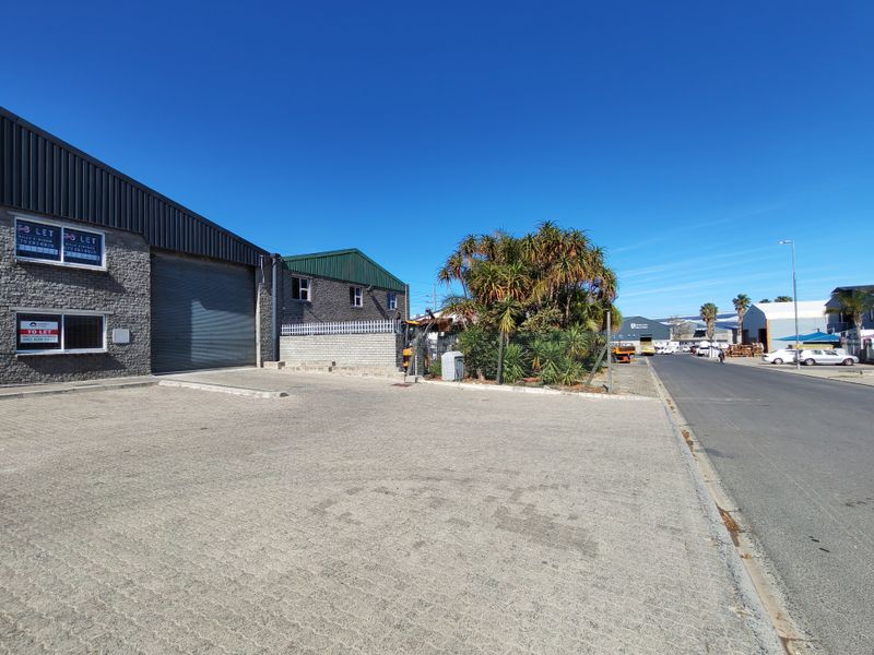 Front exterior view of an industrial property featuring a paved parking area, roller shutter door access, and secure boundary walling.