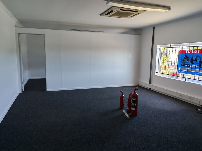 A clean, empty office space featuring carpeted flooring, recessed ceiling air conditioning, and large windows with security bars.