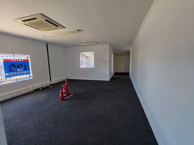 A spacious, empty office area featuring carpeted flooring, recessed ceiling air conditioning, and security-barred windows, suitable for a professional workspace.