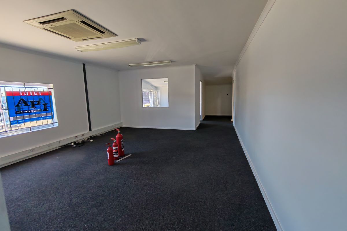 A spacious, empty office area featuring carpeted flooring, recessed ceiling air conditioning, and security-barred windows, suitable for a professional workspace.