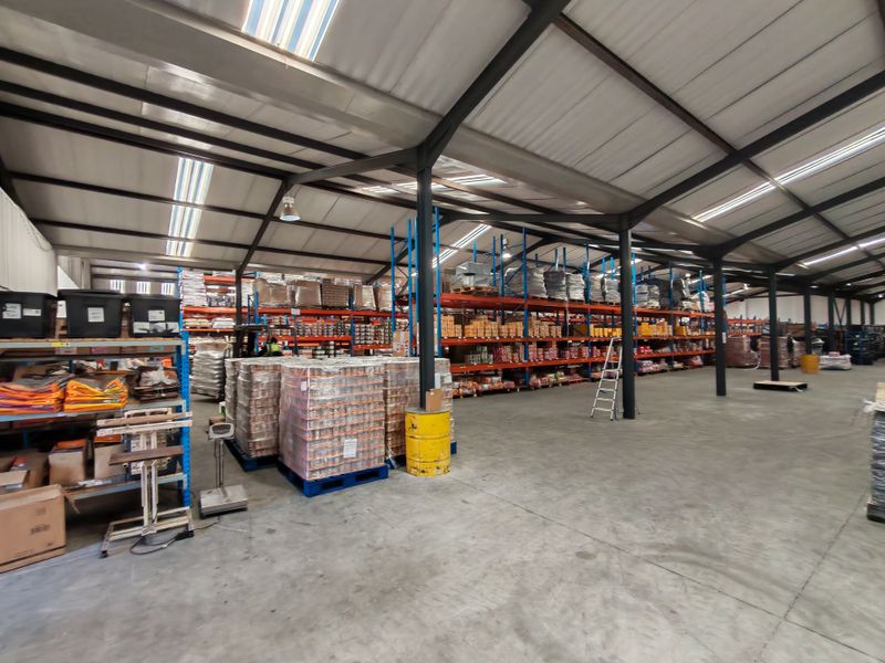 Spacious industrial warehouse featuring a steel portal frame, concrete flooring, integrated skylights, and extensive heavy-duty racking systems for storage.