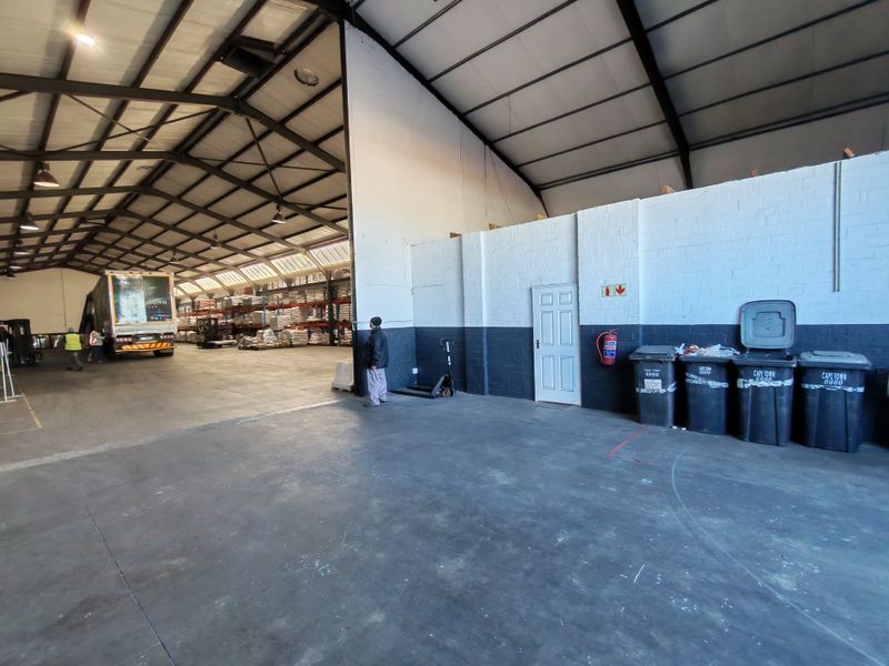Spacious industrial warehouse facility featuring high-clearance exposed steel roof trusses, durable concrete flooring, and painted brick walls suitable for logistics or storage operations.