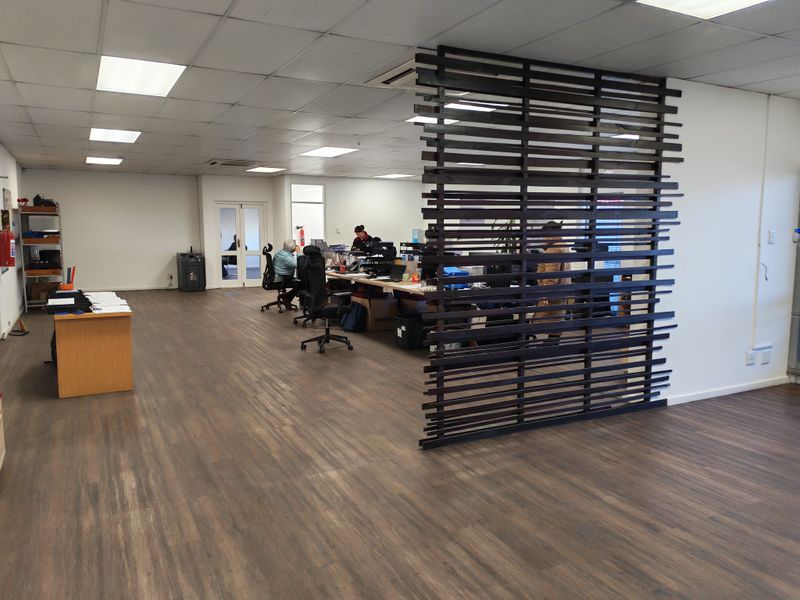 Open-plan industrial office space featuring a modern timber slat room divider, suspended ceiling with recessed lighting, and durable wood-look vinyl flooring.
