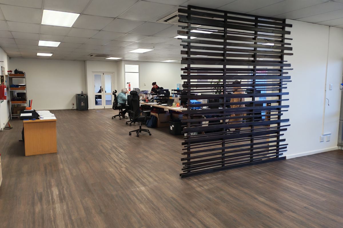 Open-plan industrial office space featuring a modern timber slat room divider, suspended ceiling with recessed lighting, and durable wood-look vinyl flooring.