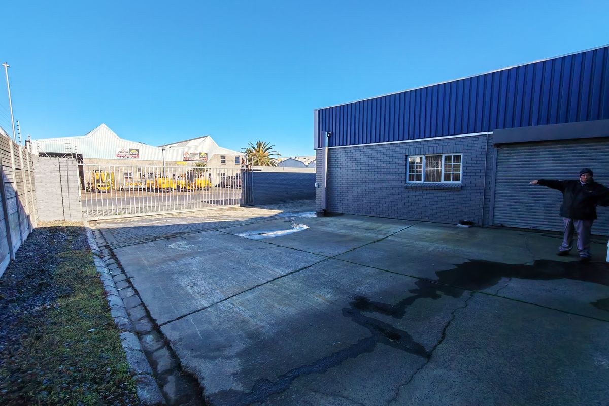 Rear industrial yard area featuring a concrete driveway, secure boundary walling, metal sliding gate, and a roller shutter door access point.