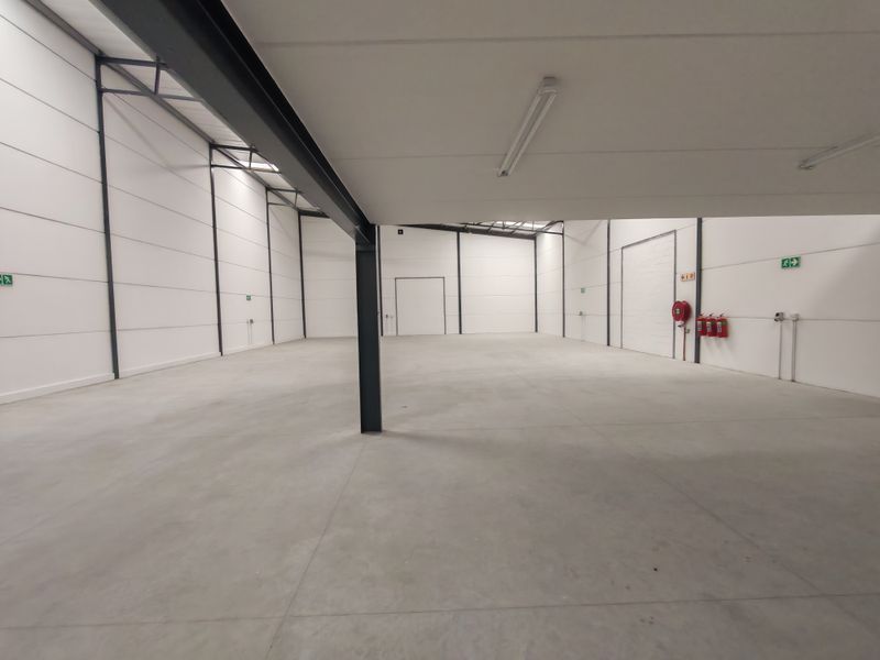 Spacious industrial warehouse unit featuring clean concrete flooring, high ceilings with integrated lighting, and essential fire safety equipment.