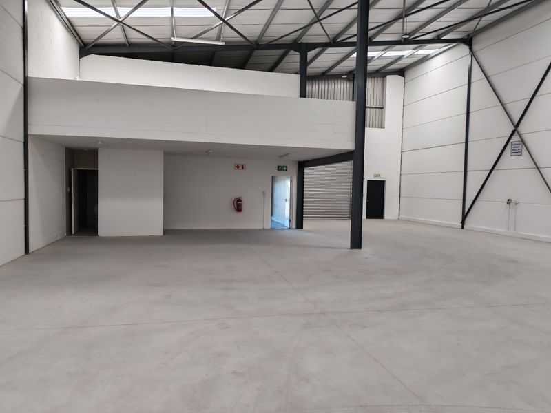 Spacious industrial warehouse unit featuring a mezzanine level, high ceilings with steel portal frame, concrete flooring, and a roller shutter door for easy access.