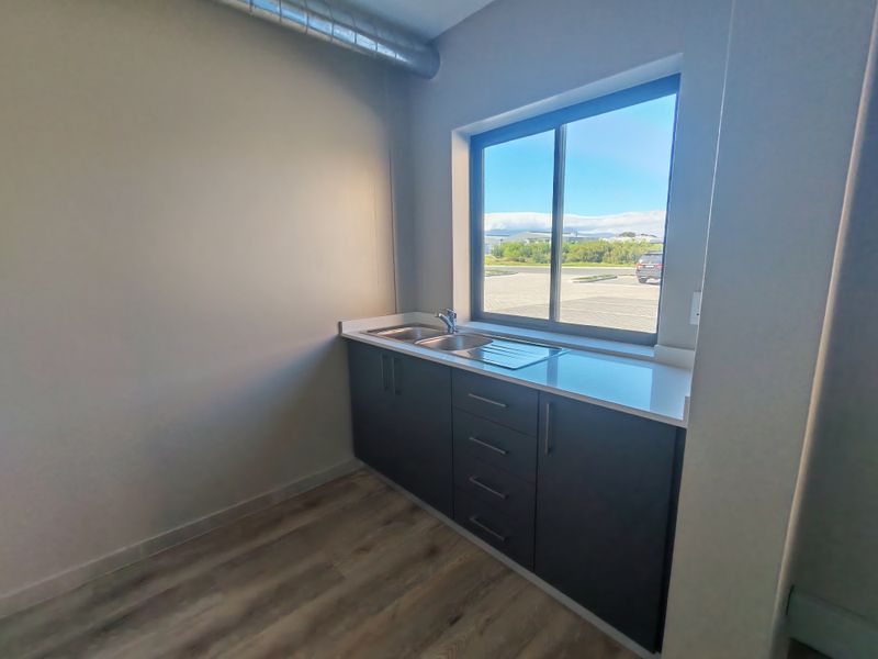 A clean, modern scullery or utility area featuring dark cabinetry, a stainless steel sink, and exposed industrial-style ducting.