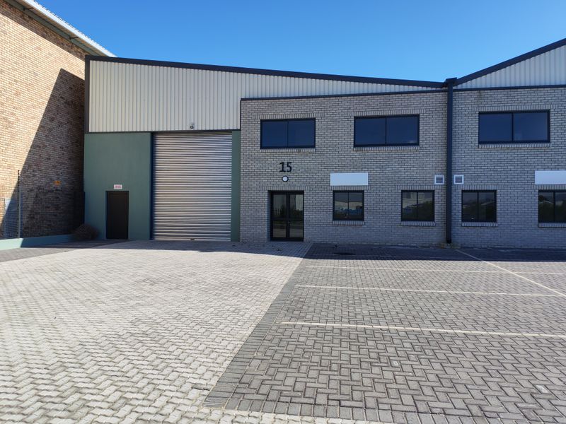 Front elevation of an industrial unit featuring a large roller shutter door, paved parking area, and modern brick and metal cladding construction.