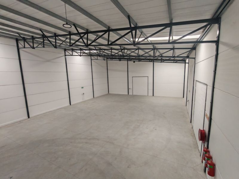 Spacious industrial warehouse unit featuring high ceilings with exposed steel trusses, insulated panel walls, polished concrete flooring, and integrated fire safety equipment.