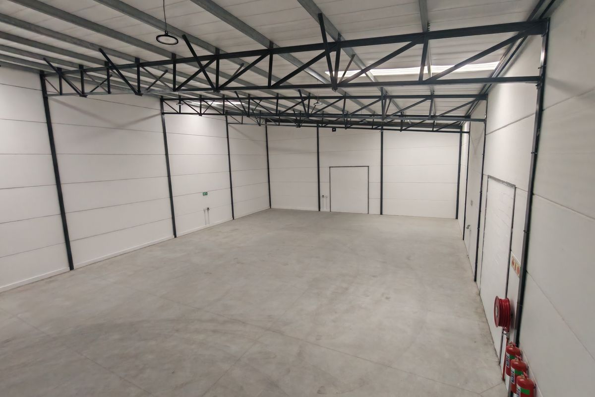 Spacious industrial warehouse unit featuring high ceilings with exposed steel trusses, insulated panel walls, polished concrete flooring, and integrated fire safety equipment.