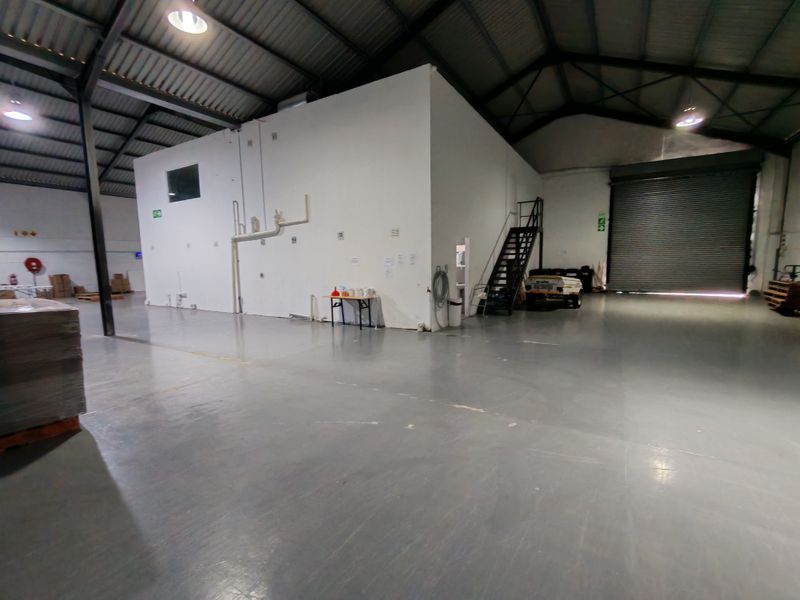 Spacious industrial warehouse unit featuring high ceilings with exposed steel trusses, a large roller shutter door, and durable epoxy-coated concrete flooring.