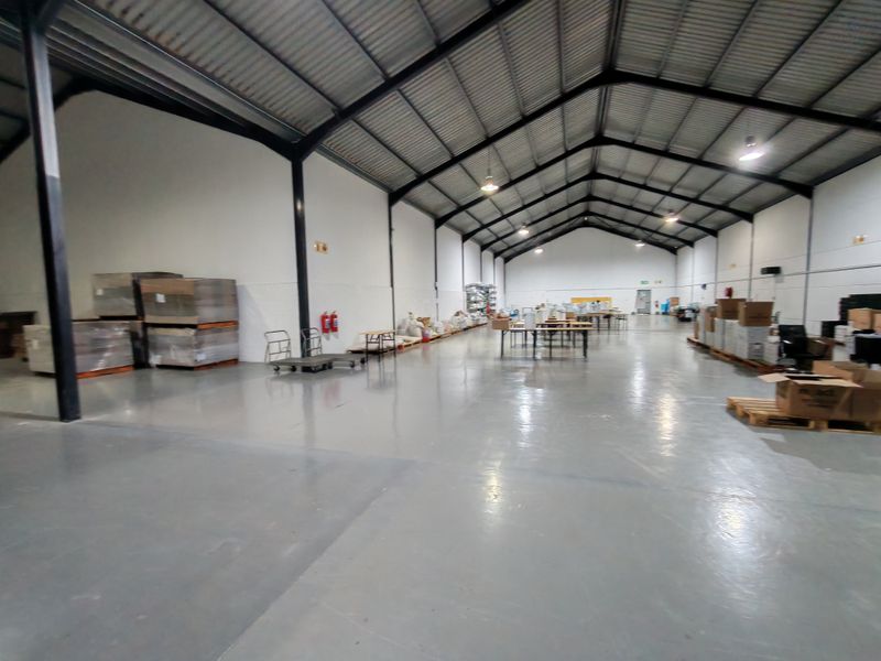 Spacious industrial warehouse featuring high ceilings with exposed steel trusses, polished epoxy flooring, and functional industrial lighting throughout the open floor plan.