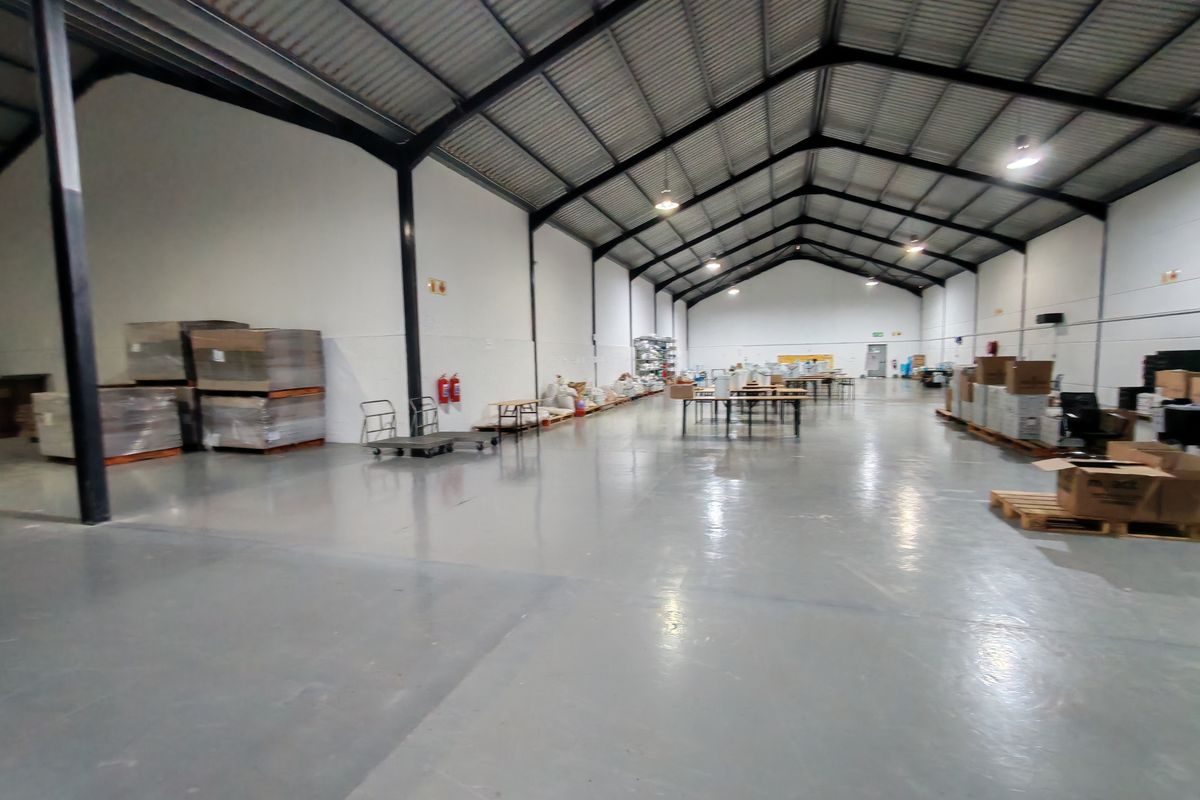 Spacious industrial warehouse featuring high ceilings with exposed steel trusses, polished epoxy flooring, and functional industrial lighting throughout the open floor plan.