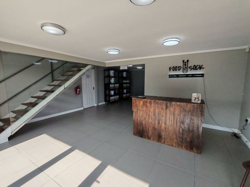 Modern industrial reception area featuring a wooden service counter, glass-railed staircase, and neutral tiled flooring in a well-maintained commercial space.