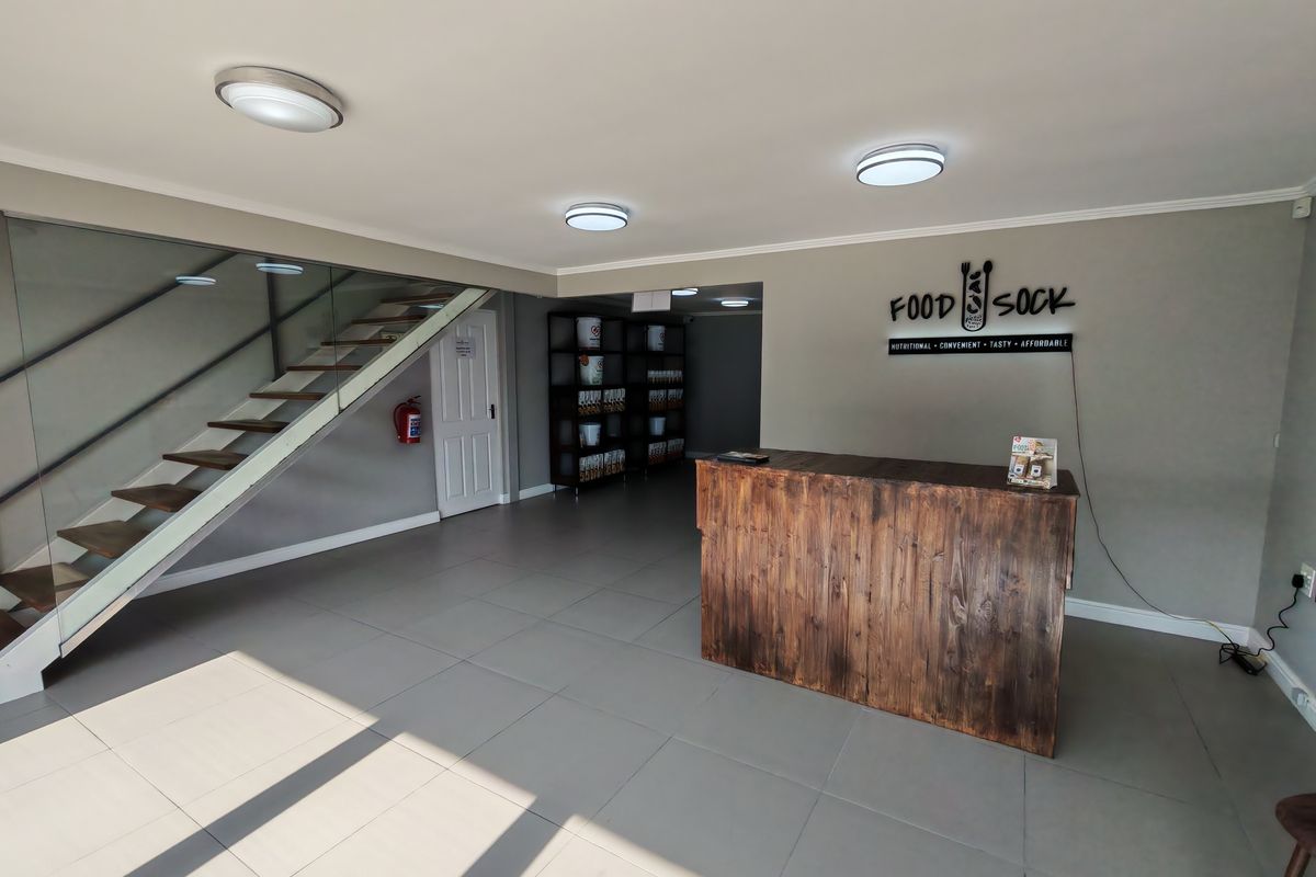 Modern industrial reception area featuring a wooden service counter, glass-railed staircase, and neutral tiled flooring in a well-maintained commercial space.