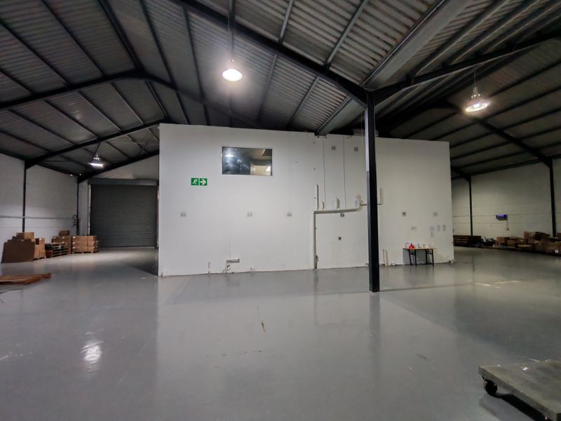 Spacious industrial warehouse unit featuring high ceilings with exposed steel trusses, polished epoxy flooring, and a secure roller shutter door for easy access.