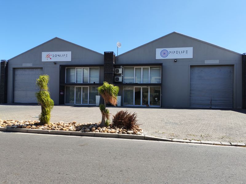 Front elevation of an industrial property featuring dual roller shutter doors, paved forecourt, and professional signage.