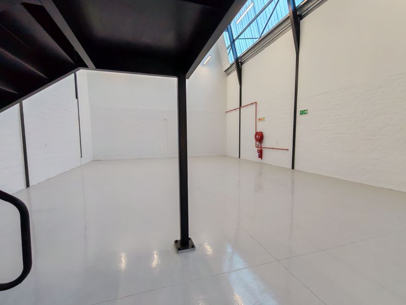 Spacious industrial unit featuring high ceilings, polished epoxy flooring, exposed steel structural elements, and integrated fire safety equipment.