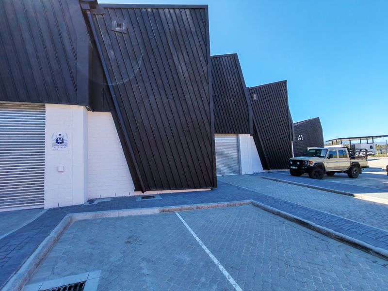 Modern industrial warehouse units featuring striking black metal cladding, roller shutter doors, and paved exterior parking area.