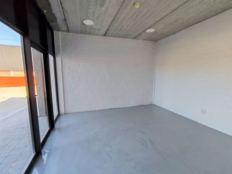 A clean, modern industrial-style office space featuring exposed concrete ceilings, painted brick walls, and durable epoxy flooring with large glass entrance doors.