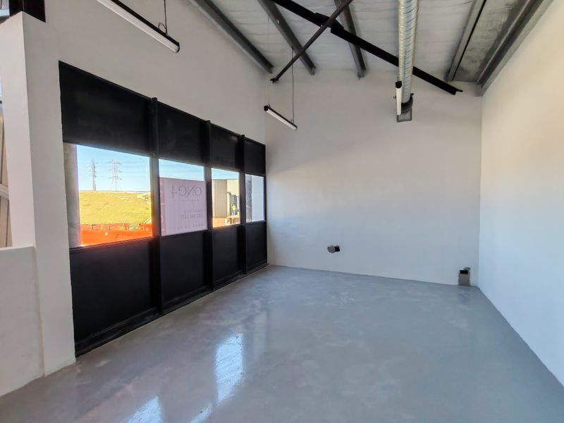 A modern, empty industrial office space featuring polished epoxy floors, exposed steel roof trusses, and large black-framed windows providing ample natural light.