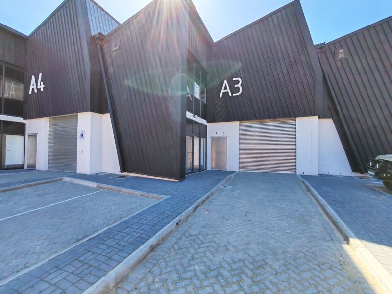 Modern industrial unit exterior featuring dark corrugated metal cladding, paved driveway access, and secure roller shutter doors.